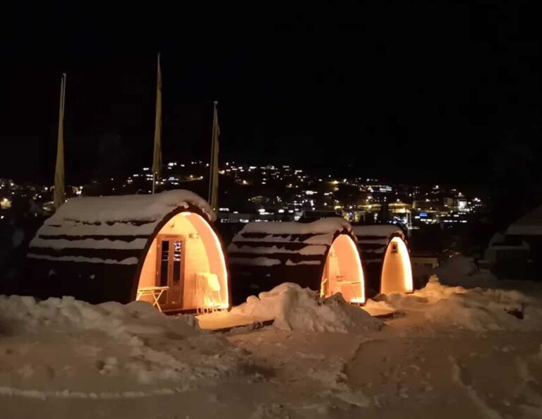 Camping-Pods bei Nacht im Schnee über dem Ort Scuol