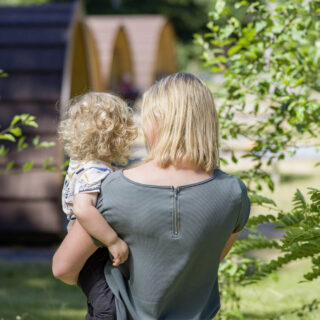 Frau mit Kind auf dem Arm vor Camping PODs im Grünen
